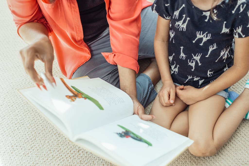 A mother and daughter sit on the floor, engaged in reading a colorful children's book.