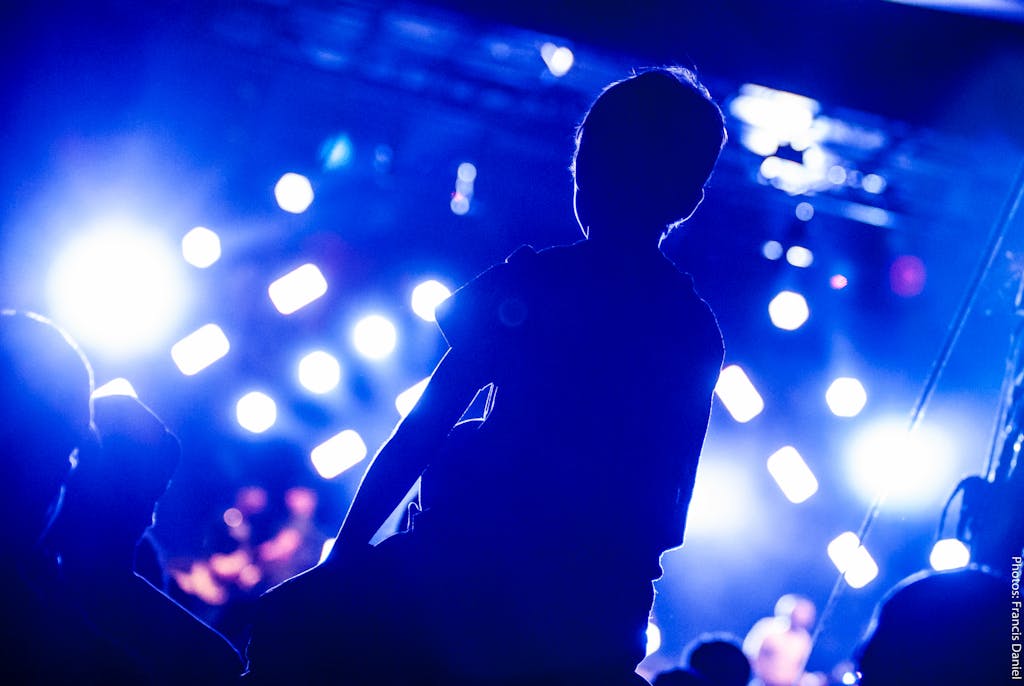 Dynamic concert scene capturing audience silhouette against bright stage lights.