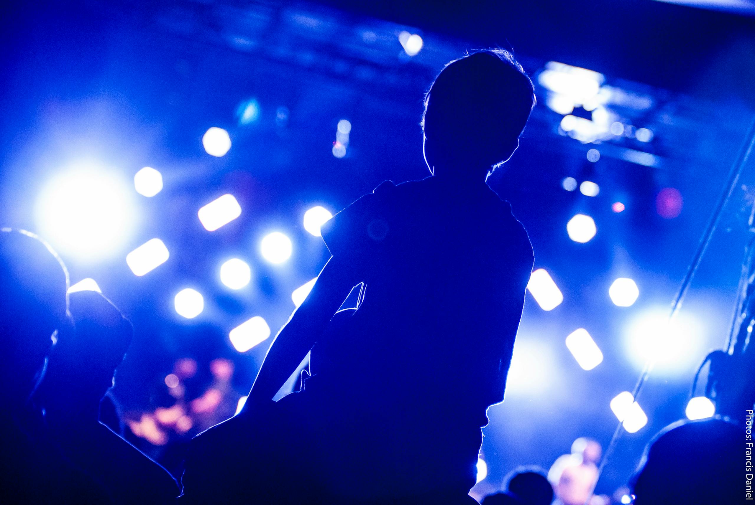 Dynamic concert scene capturing audience silhouette against bright stage lights.